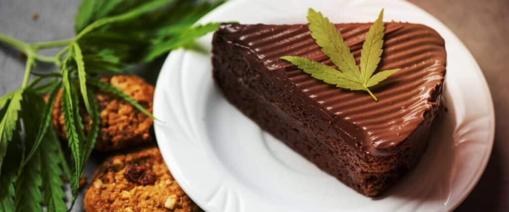 Indulge in a decadent heart-shaped chocolate cake topped with a fresh cannabis leaf, accompanied by cannabis-infused cookies. Perfect for exploring gourmet cannabis edibles in a stylish presentation.