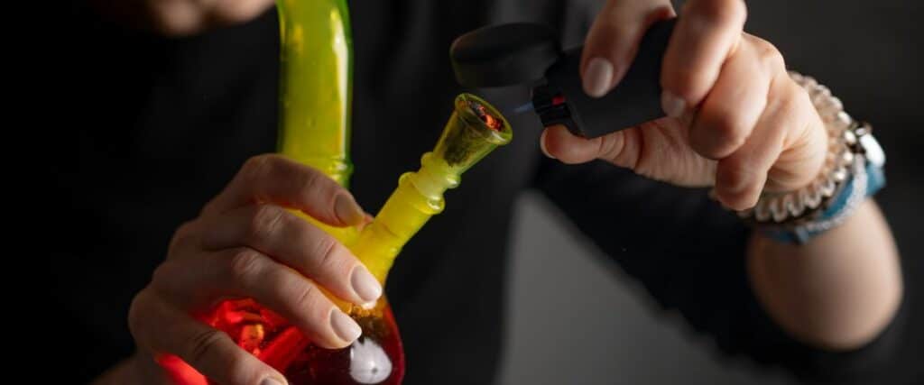 A person lighting a colorful bong with a black lighter.