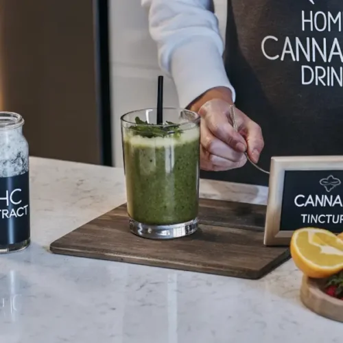 Person preparing a cannabis smoothie with THC extract and fresh herbs in a modern kitchen
