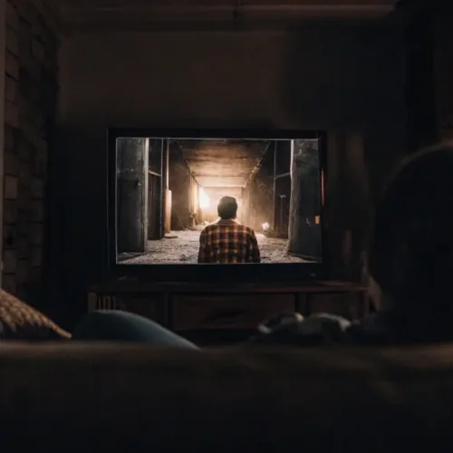 Person with back to camera watching a TV in a dark room, showing a figure in a tunnel.