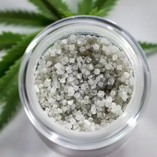 THCA isolate crystals in a small glass jar on a wooden table, surrounded by natural elements and sunlight.