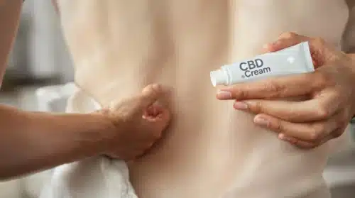 Person applying CBD cream to the back for soothing relief from hemorrhoid pain.