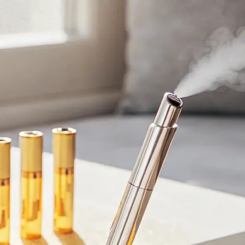 A person using a sleek gold vape pen to inhale cannabis oil, with multiple gold cartridges on a table.